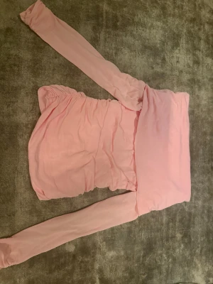 Ljusrosa offshoulder kortklänning - Supersöt ljusrosa kortklänning med offshoulder och långa ärmar. Klänningen har rynkade detaljer på sidorna och är figurnära med en mjuk, stretchig känsla. Perfekt för dig som vill ha en feminin och trendig look.