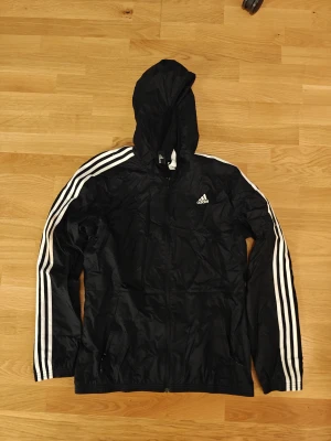 Adidas Vindjacka Storlek M - Svart vindjacka från Adidas. Mycket fint begagnat skick. Storlek Medium