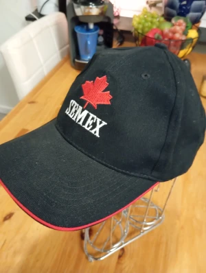 Ny keps Svart Semex - Snygg svart keps Semex med broderat rött lönnlöv och vit text framtill. Röd kant på skärmen och justerbar rem med 'SWEDEN' broderat baktill. Tillverkad i bomullstyg, perfekt för dig som gillar unik stil och internationella vibbar.