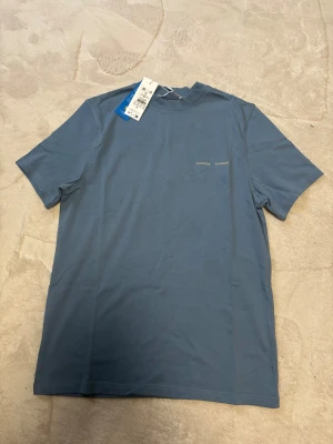 T-shirt från Samsøe Samsøe - Snygg blå t-shirt från Samsøe Samsøe med diskret logga på bröstet. Perfekt för dig som gillar stilrena och enkla plagg med modern vibe. 