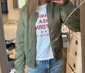 Olivgrön bomberjacka från Bik Bok - Snygg olivgrön bomberjacka från Bik Bok i storlek S. Jackan har en cool orange insida, silverfärgad dragkedja framtill och på ärmen, samt ribbade muddar vid krage och ärmslut. Perfekt för dig som vill ha en klassisk streetstil med lite edge.