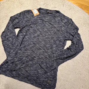 Mörkblå stickad tröja Jack & Jones - Snygg mörkblå stickad tröja från Jack & Jones Originals i storlek small. Tröjan har ett melerat mönster i blått och vitt, rund hals och långa ärmar. Perfekt för dig som gillar enkel och stilren design med en chill vibe.