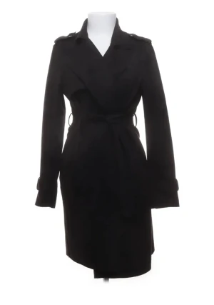 Trenchcoat  - Snygg svart trenchcoat med klassisk krage och bälte i midjan. Jackan har långa ärmar med spänndetaljer vid mudden och axelklaffar som ger en cool siluett. Perfekt för dig som gillar stilrena och tidlösa plagg.