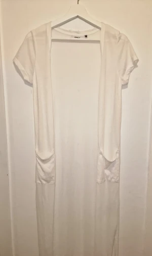 Viit kofta - Vit, ankellång kofta med korta ärmar och fickor fram. Perfekt att bära lager på lager. Aldrig använd, endast tvättad. 