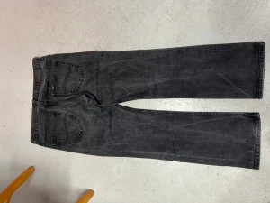 Svarta straight jeans från Lee - Snygga svarta jeans från Lee med klassisk femficksdesign och raka ben. Jeansen har Lee-logga på bakfickan och metallknappar framtill. Materialet är slitstarkt denim och färgen är mörkgrå/svart med lätt tvättad look. Perfekt för dig som gillar tidlös stil. Passar som 32