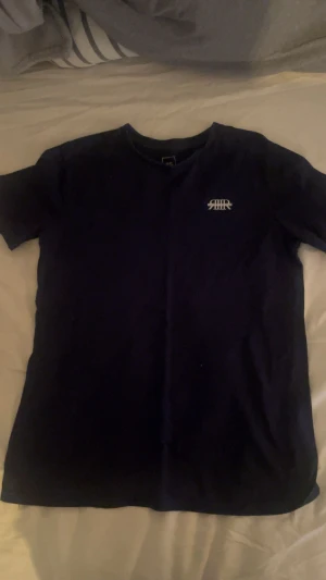 Mörkblå t-shirt från River Island - Snygg mörkblå t-shirt från River Island med vit broderad logga på bröstet. Modellen är slim fit och har klassisk rund hals och korta ärmar. Perfekt för en clean och stilren look.