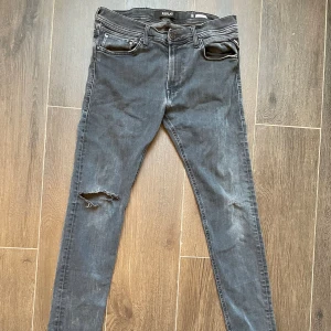 Replay Jondrill svarta - Svarta Replay Jondrill jeans i skinny fit med slitningar på ena benet. Klassisk femficksdesign, snygga detaljer och en cool tvättad look. Passar dig som gillar smalare siluett och streetstyle. Materialet är stretchigt jeans för extra komfort. Det är ett hål vid knät därav det låga priset.