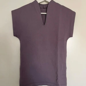 Lila ribbad topp från New Apparel - Säljer en lila ribbad träningstopp från New Apparel i storlek S. Toppen har en v-ringad hals och är ärmlös med en lite tightare passform. Materialet är mjukt och stretchigt, perfekt för dig som gillar enkel och bekväm topp till träning eller vardags. 