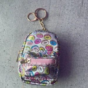 Mini ryggsäck med nyckelring - Söt liten ryggsäck i silverfärgad syntet med färgglatt donut-mönster i rosa, blått och gult. Väskan har rosa och guldiga dragkedjor och ett  litet ytterfack. Perfekt som accessoar eller för att ha småsaker i. Ungefär 11 cm hög och 9cm bred. (Var snäll och lajka om du är intresserad)💞