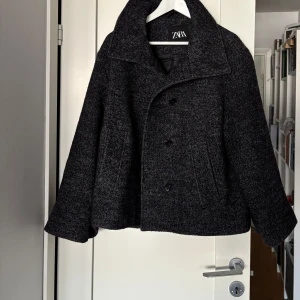 Kort ull kappa från Zara - Säljer en grå/svart melerad fiskbensmönstrad ull kappa från Zara. Är fodrad och i ull blandning så den är varm och skön och man kan ha hela vintern! Så fin och u jättefint skick. Nypris 1500k. I storlek S men passar M