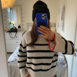 Randig stickad tröja med röd kant - Säljer en ribbstickad tröja i beige med svarta ränder och coola röda detaljer vid ärmslut och nederkant. Köp från Zara och är i storlek S💓 pris kan diskuteras