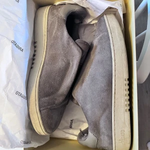Grå mocka dice lascless  sneakers från Arigato - Snygga slip-on sneakers från Arigato i grå mocka med elastisk panel över vristen för enkel påtagning. Skorna har rund tå, platt sula med tydlig Arigato-logga undertill och detaljer i ljusgrått skinn vid hälen. Perfekt för dig som gillar minimalistisk och clean stil.(pris kan diskuteras)!!!!!!!! Lite skitiga så kan behöva en tvätt annars en bra sko för bra pris lite slitna vid hälen också 