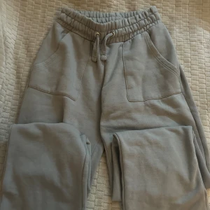 Grå mjukisbyxor med snörning samt matchande kofta - Grå mjukisbyxor med bred resår och snörning i midjan. Byxorna har stora fickor fram och två bakfickor, tillverkade i mjukt bomullsmaterial. Perfekta för chill eller träning, loose fit och enkel stil. Med matchande kofta i storlek M