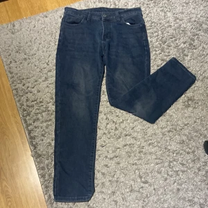 Mörkblå jeansbyxor i storlek 28 - Snygga mörkblå jeansbyxor med klassisk femficksdesign och raka ben. Jeansen har normal passform och är tillverkade i ett mjukt och slitstarkt bomullsmaterial med lite stretch. Perfekta för dig som gillar en enkel och stilren look.