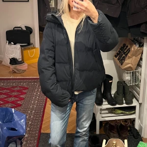 Svart pufferjacka med huva från UNIQLO - Säljer en svart pufferjacka med huva och dragkedja framtill från UNIQLO.  Perfekta vinterjackan!!❤️. Den är vadderad och har två sidofickor. Den har lite fläckar som jag kan skicka bild på om det önskas men inget man tänker på!