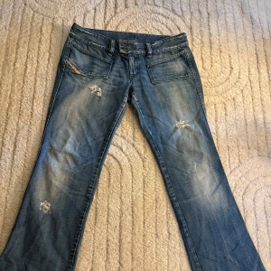 Blå jeans med slitningar   - Snygga blå jeans i klassisk tvätt med slitna detaljer och boutcut. Modellen har framfickor med Diesel Industry-logga och bakfickor med markerade sömmar. Jeansen är tillverkade i Italien och har en normal passform. Pris kan diskuteras 