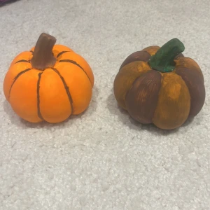 Dekorativa konstgjorda pumpor (2-pack) - Två handmålade dekorationspumpor i betång. perfekta för höst- eller Halloweenpynt. En orange med bruna detaljer och en brun/orange med grön stjälk. Mycket fint skick, inga synliga skador eller slitage.