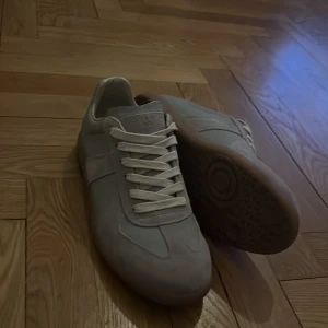 Grå sneakers med mockadetaljer - PRIS KAN SÄNKAS VID SNABB AFFÄR. Snygga grå sneakers med vita snören och beige gummisula. Ovandelen har både släta och mockadetaljer som ger en clean och stilren look. Rund tå och platt sula gör dem sköna att bära. Perfekta för dig som gillar minimalistisk stil. Har ingen box och de lite smuts på ena skon men går att få bort använda max 3 gånger storlek är 46 men passar 45 med