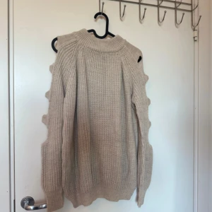 Beige stickad tröja med coola detaljer - Säljer en beige stickad tröja med långärmade ärmar och unika utstickande detaljer längs ärmsidorna. Tröjan har en högre hals och grovstickad struktur som ger en chill vibe. Perfekt för dig som gillar att sticka ut med din stil.
