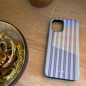 Burga Tough MagSafe Lowkey iPhone-skal  - Stilrent Burga Tough MagSafe-skal i Lowkey-design med blå ränder. Dubbla lager: silikoninsida och hård exteriör ger extra skydd. Passar iPhone, mycket gott skick utan synligt slitage. Perfekt för dig som vill kombinera stil och säkerhet.