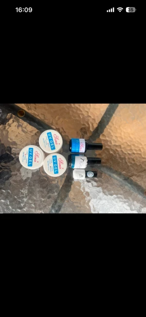 Sina UV gel och nagelprodukter - Ett kit med tre burkar UV gel från Sina och fyra flaskor nagelprodukter, inklusive top coat och primer. UV gelen är vit med blå etikett, flaskorna är svarta och vita med olika etiketter. Perfekt för dig som gillar att fixa naglarna hemma.