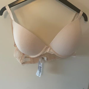 Beige  bh från Censored - Säljer en beige  bh från Censored med   spetsdetaljer på sidorna. Bh:n har justerbara axelband och en liten rosett framtill. Perfekt för dig som vill ha en bekväm och snygg bh med extra stöd.