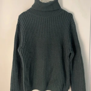 Mörkgrå stickad polotröja - Snygg mörkgrå stickad polotröja med grov struktur och hög krage. Tröjan har långärmade och en loose passform som ger en chill vibe. Perfekt för att hålla sig varm och se cool ut under kalla dagar. Passar dig som gillar enkel och stilren design.