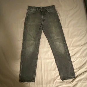 Jack and Jones Jeans - Snygga grå jeansbyxor i straight fit med klassisk femficksdesign och knappgylf. Byxorna är från Jack and Jones och knappt använda. Storlek 31/32.