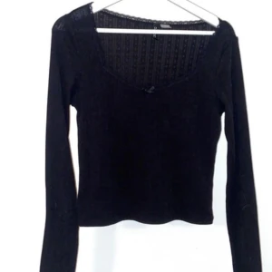 Svart långärmad blus från hm - Supersöt svart långärmad blus från hm med diskret spetskant vid halsringningen och liten rosett framtill. Toppens tyg har ett subtilt mönster och är croppad i modellen. Perfekt för dig som gillar stilrena och feminina detaljer.