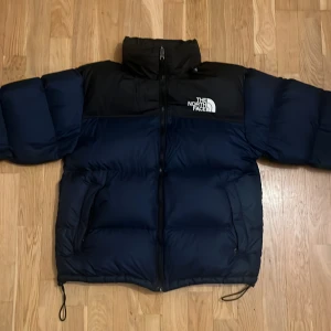 The North Face 700 svart/blå pufferjacka - Säljer en pufferjacka från The North Face i svart och mörkblå, säljer eftersom det inte passar min stil längre. Jackan är fylld med dun och har justerbara snören vid nederkant. Perfekt för kalla dagar då den håller dig varm.
