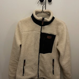 Jacka - Pilejacka i gräddvit färg med svarta och bruna detaljer. Fint skick en liten fläck men går nog bort med en tvätt