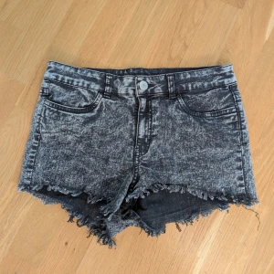 Grå denimshorts från H&M Divided - Snygga grå denimshorts från H&M Divided med cool tvättad look och råa, fransiga kanter. Klassisk femficksmodell med knapp och dragkedja fram. Materialet är en mix av bomull, polyester och elastan för skön stretch. Perfekta för dig som gillar edgy streetstil.