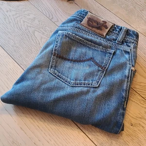 Jacob Cohen jeans modell 688 - Snygga blå jeans från Jacob Cohen i klassisk modell 688. Jeansen har fem fickor, kontrastsömmar och ett brunt läderpatch med logga bak. Materialet är mjukt denim och passformen är normal. Perfekt för dig som gillar stilrena och tidlösa jeans. Tyvärr är båda framfickorna trasiga därav det låga priset. Det går att laga för en liten peng men jag själv orkar inte det därav säljs de. De går även att ha på sig som de är nu då det inte finns några slitningar på jeansen i sig.