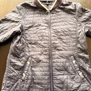 Grå jacka Ilse Jacobsen - Snygg grå jacka från Ilse Jacobsen med ribbad krage och dragkedja framtill. Jackan har två fickor med tryckknappar och ett stilrent metallmärke på sidan. Perfekt för dig som gillar en clean och sportig look.