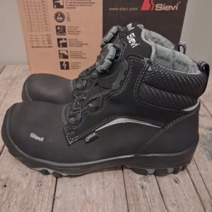 Svarta kängor från Sievi med BOA - Svarta kängor från Sievi med BOA-snörningssystem och robust, mönstrad sula för extra grepp. Ovandelen har detaljer i grått och reflekterande inslag, samt vadderad mesh vid ankeln. Skorna är tillverkade i slitstarkt syntetmaterial och har en sportig, modern look. Ny pris 3500 kr