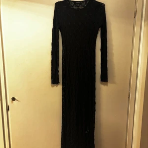 Svart spetsklänning från Stradivarius - Supersnygg lång svart spetsklänning från Stradivarius med figurnära passform och långa ärmar. Klänningen har ett transparent spetsmönster som ger en cool och elegant vibe och den går hela vägen ner på mig som är 166