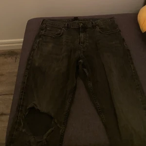 Gråa skinny jeans från H&M 32/32 - Gråa skinny fit jeans från H&M i storlek 32/32. Jeansen har en tight passform och ett stort hål vid ena knät för en trendig, sliten look. Klassisk femficksmodell med dragkedja och knapp. Perfekta för dig som gillar en edgy stil.
