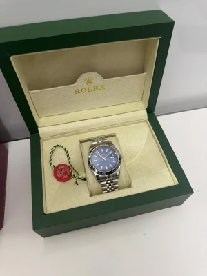 R0lex Datejust blå urtavla stål - R0lex Datejust med blå urtavla. Klockan har jubilee-armband och datumvisning. Den eleganta kombon av silverfärgen och blått gör den riktigt stilren. medföljer extra länkar och kommer i originalbox 