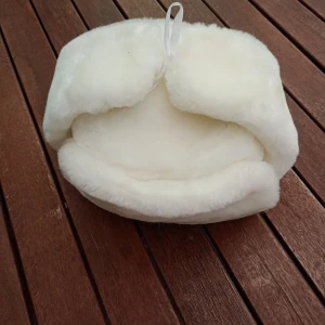 Vit päls mössa fuskpäls stl 56 - Säljer en klassisk vit ushanka från Korona, tillverkad i Sovjetunionen 1991. Hatten har mjuk pälsimitation och quiltad insida för extra värme. Öronlapparna kan knytas upp på toppen eller bäras nedfällda. Perfekt för kalla vinterdagar.