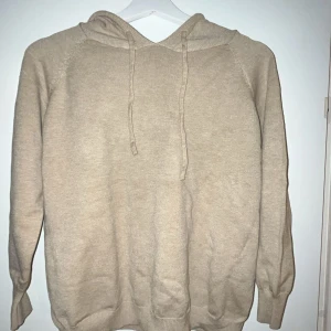 Beige merinoull hoodie med huva - Mysig beige merinoull hoodie med huva och snörning framtill. Tröjan har långa ärmar. Den är 40cm bred 50cm lång. Perfekt för lager-på-lager och chill dagar.