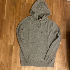 Grå hoodie från Morris Stockholm - Klassisk grå hoodie från Morris Stockholm med broderad svart logga på bröstet. Aldrig använd med prislapp! Tröjan har huva med snörning, Ordinare pris:2000kr köpt från Morris! 
