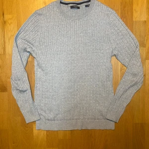  ribbad tröja Jack & Jones L - Snygg grå stickad tröja från Jack & Jones Premium i storlek L. Tröjan har ett ribbat mönster och rund halsringning, perfekt att bära över en skjorta. Långärmad och med mjuk känsla, passar dig som gillar stilrena och klassiska plagg.