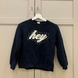 Mörkblå sweatshirt med pärlor Zara - Mörkblå sweatshirt från Zara Kids med  'hey'-tryck framtill dekorerat med pärlor. Tröjan har rund hals, ribbade muddar och lång ärm. Tröjan är i fint skick och är väldigt skön💕