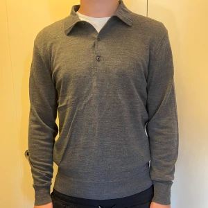 Grå pikétröja från Uniqlo - Säljer en stilren grå pikétröja från Uniqlo med klassisk krage och två knappar framtill. Tröjan är långärmad och har en mjuk, stickad känsla som gör den skön att bära. Perfekt för dig som gillar enkel och clean stil.