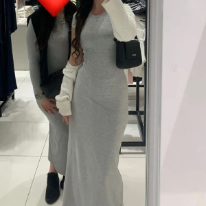 Grå långklänning i bomull - Säljer en enkel och stilren grå långklänning i mjuk bomull. Klänningen har en rund halsringning och är kortärmad, med en figurnära passform som ger en snygg siluett. Perfekt för dig som gillar minimalistisk och clean stil.