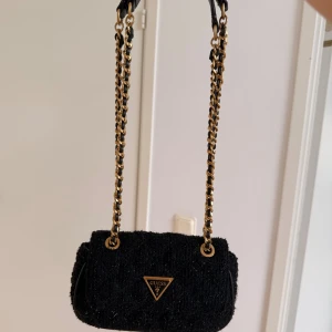 Svart axelväska från Guess med kedja - Snygg svart axelväska från Guess. Kommer dessvärre inte till användning. Nyskick