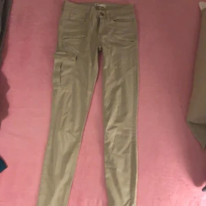 Beige cargopants från Gina Tricot - Säljer ett par snygga beige cargopants från Gina Tricot, modell Perfect Jeans. Byxorna har flera fickor med dragkedja och en klassisk cargoficka. Perfekt för dig som gillar streetstyle och praktiska detaljer.