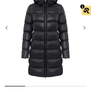 Äkta Svart lång blank dunjacka från colmar - Säljer en svart, lång dunjacka från colmar med huva och markerad logga på ärmen. Jackan har quiltad design, dragkedja framtill och är perfekt för kalla dagar. Den är stilren och har en snygg, figurnära passform som håller dig varm hela vintern.