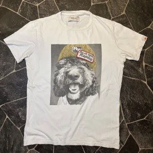 Replay T-shirt - Säljer en vit t-shirt från Replay med ett stort tryck på framsidan av en hund med mössa och texten 'Do it with Replay'. T-shirten har rund hals och korta ärmar, perfekt för dig som gillar coola och unika motiv.