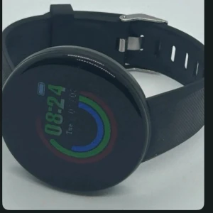 Svart rund smartklocka med färgdisplay - Säljer en stilren svart smartklocka med rund form och digital färgdisplay. Klockan har silikonarmband och metallspänne, samt visar tid, datum och aktivitetsringar i grönt, blått och rött. Perfekt för dig som gillar teknik och vill ha koll på stegen.